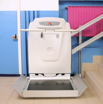 An inclined wheelchair platform lift with ramps lowered at the bottom of a tiled staircase in an indoor public or commercial building space.